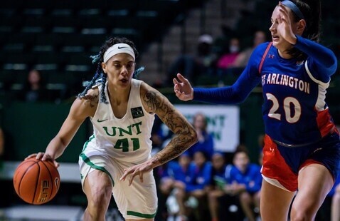 UNT basketball player dribbling a basketball next to a player from an opposing team