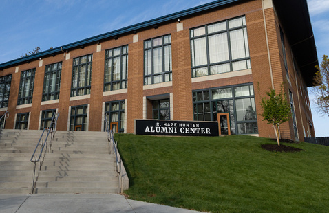 The Hunter Alumni Center is a brown brick building with a navy roof, and has taller windows throughout the building. 