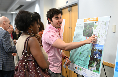 Student pointing at his poster presentation while talking to someone