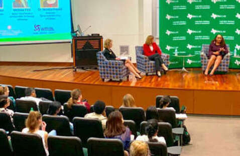 An audience listens to panelists speaking on stage. 
