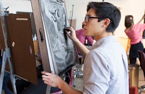 A student draws a black and white image on a canvas.