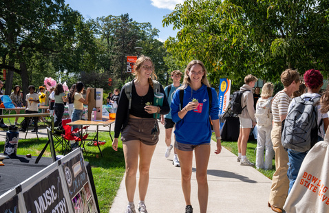 two individuals talking and waslking through on the quad by a table at campus fest