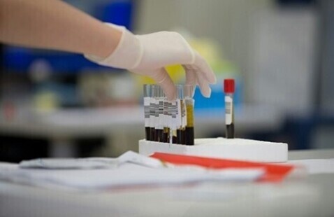 gloved hand picks up a vial of blood.