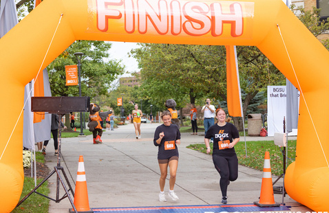 2 students running in a 5k race under the finish line