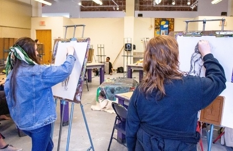 Two people in art room drawing on canvas with easel