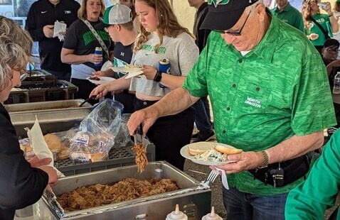 A person in UND Fighting Hawks green attire serves food during the tailgate event.