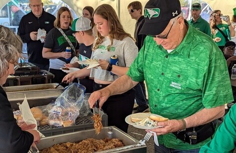 A person in UND Fighting Hawks green attire serves food during the tailgate event.