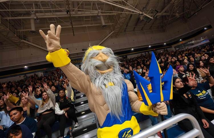 King Triton mascot in crowded stadium raising Trident hand sign