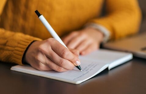picture of hand with a pen writing in a notebook on a table