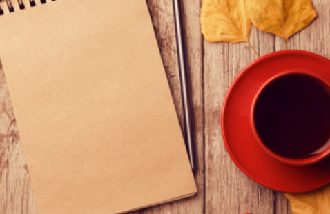 notebook and orange cup of coffee surrounded by leaves