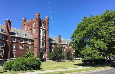 A classical brick building that looks like a castle, with trees and a lawn in front