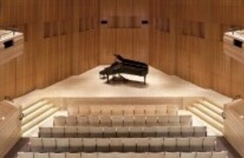 piano in the center of a stage with empty rows of seats in front of it.