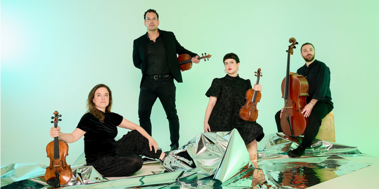 Two men and two women pose in front of green backdrop with violins