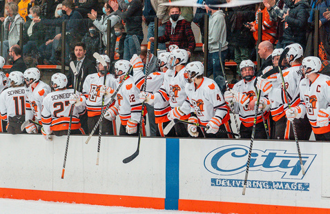hockey players sitting along the wall watching the ice 