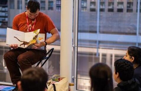 A man reads a picture book to a group of families in a gallery. 