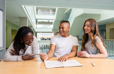 Three students sitting at a table laughing and studying