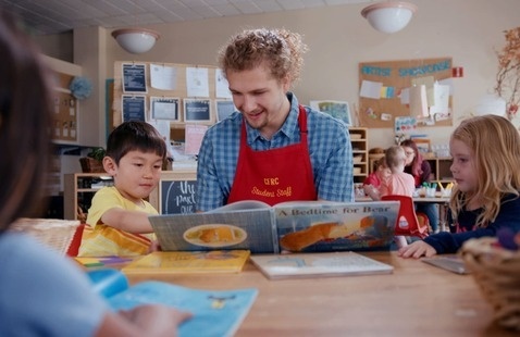 Student reading a book with two young kids in a classroom