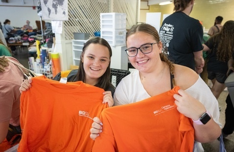 students smiling at a camera while holding up tshirts