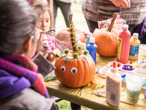 Family and Friends attendees decorate pumpkins at a table, craft supplies on the table.
