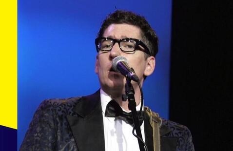 Inside  the Shape of a yellow bowtie are the words, in capital letters, Buddy Holly: OH BOY, with an exclaimation mark after the word Boy.  There is a man in a black suitcoat, white shirt and black bowtie standing, mid-chest and up, in front of a microphone on the right side of the photo.  The words under the yellow bowtie say Accoring to Buddy Holly's Crickets: in quotation marks This is about as close to the real deal y'all are going to get."  The background is blue. 