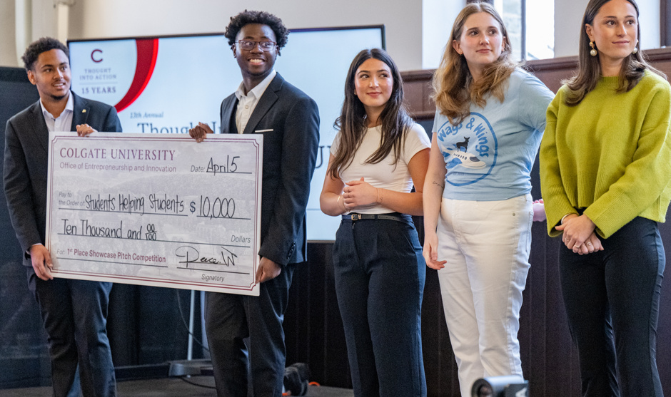Student participants in the 2025 competition stand on stage while two of them hold a giant check.