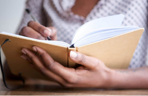 Hands holding and writing in a journal.