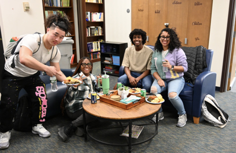 Group of four students sit in The Kearns Center living room for an event. 