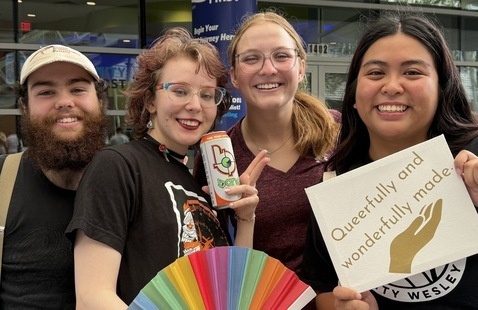 Four students smiling holding a rainbow colored fan