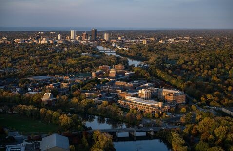 An aerial shot of the University of Rochester campus with the Rochester skyline in the background