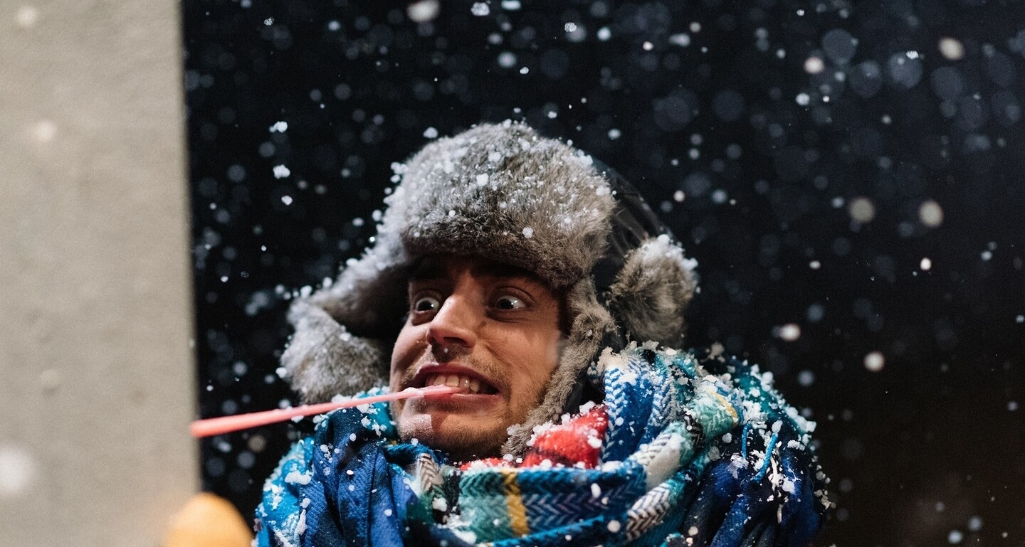 Performer in winter clothes with his tongue stuck to a pole in falling snow. 