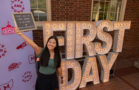 Student holding up a sign in front of large light up "First day" letters
