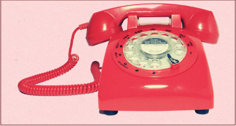 The photo displays a red dial phone in front of a pale pink solid background. 