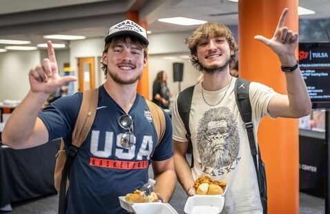 Two male students stand smiling holding styrofoam containers of food
