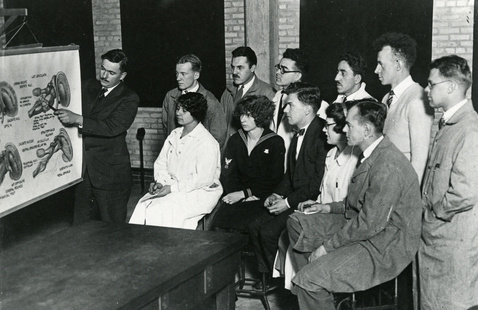 historic photo of a professor lecturing to a group of students.