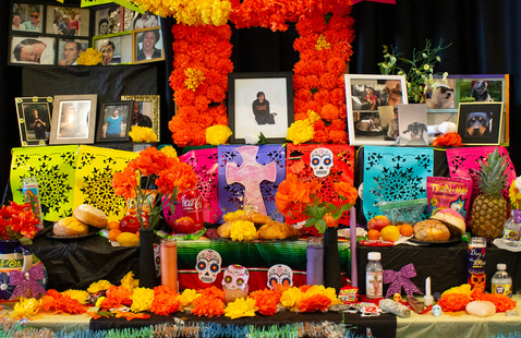 Día de los Muertos altar with marigolds, papel picado, photos, sugar skulls, candles, and food offerings.