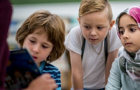 Three children sitting and looking attentively at a open book held by another person