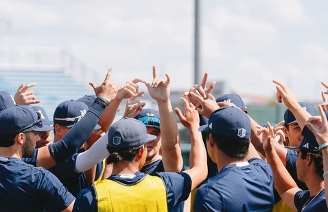 University of Nevada, Reno Men's Baseball team huddled with Wolf Pack hands in the air.