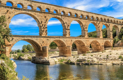 multiple stone arches spanning a river under a bright blue sky.