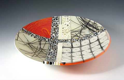 A handmade glass plate decorated with various patterns in cream, red, and black.