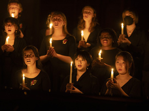 Vespers performance, students in black clothing hold candles, singing.