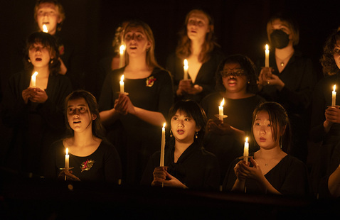 Vespers performance, students in black clothing hold candles, singing.