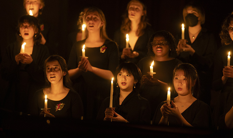 Vespers performance, students in black clothing hold candles, singing.