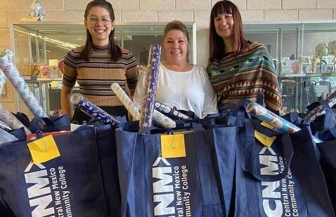 Three people smile in front of CNM branded gift bags 