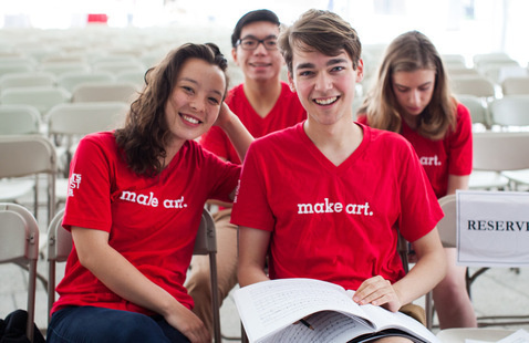Smiling students, seated, wearing red t-shirts with the words, "make art" on the front.