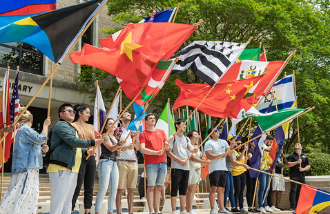 A group of students outdoors holding flags on poles of various countries.