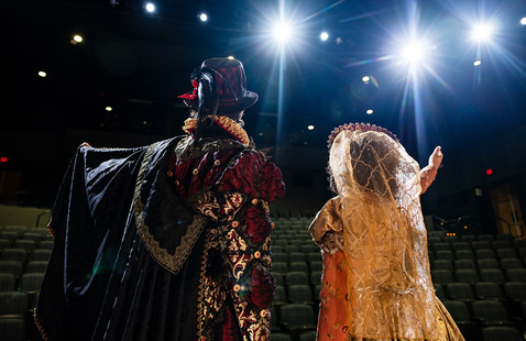 Back view of two theatre performers in Shakespeare theme attired on a stage.