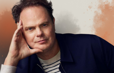 an image of rainn wilson posing with an orange faded background