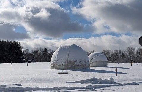 Two white telescope domes in a snowy field. 