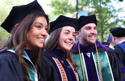 Three students dressed in commencement regalia posing for a photo.