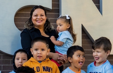 Teacher holds young child along with other children in her class